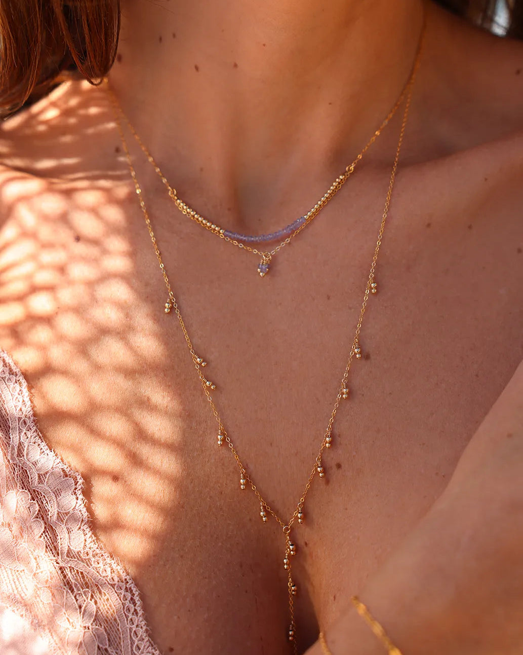 Model wearing doubl chain necklace with a row of radiant Tanzanite gems and gold accent beads