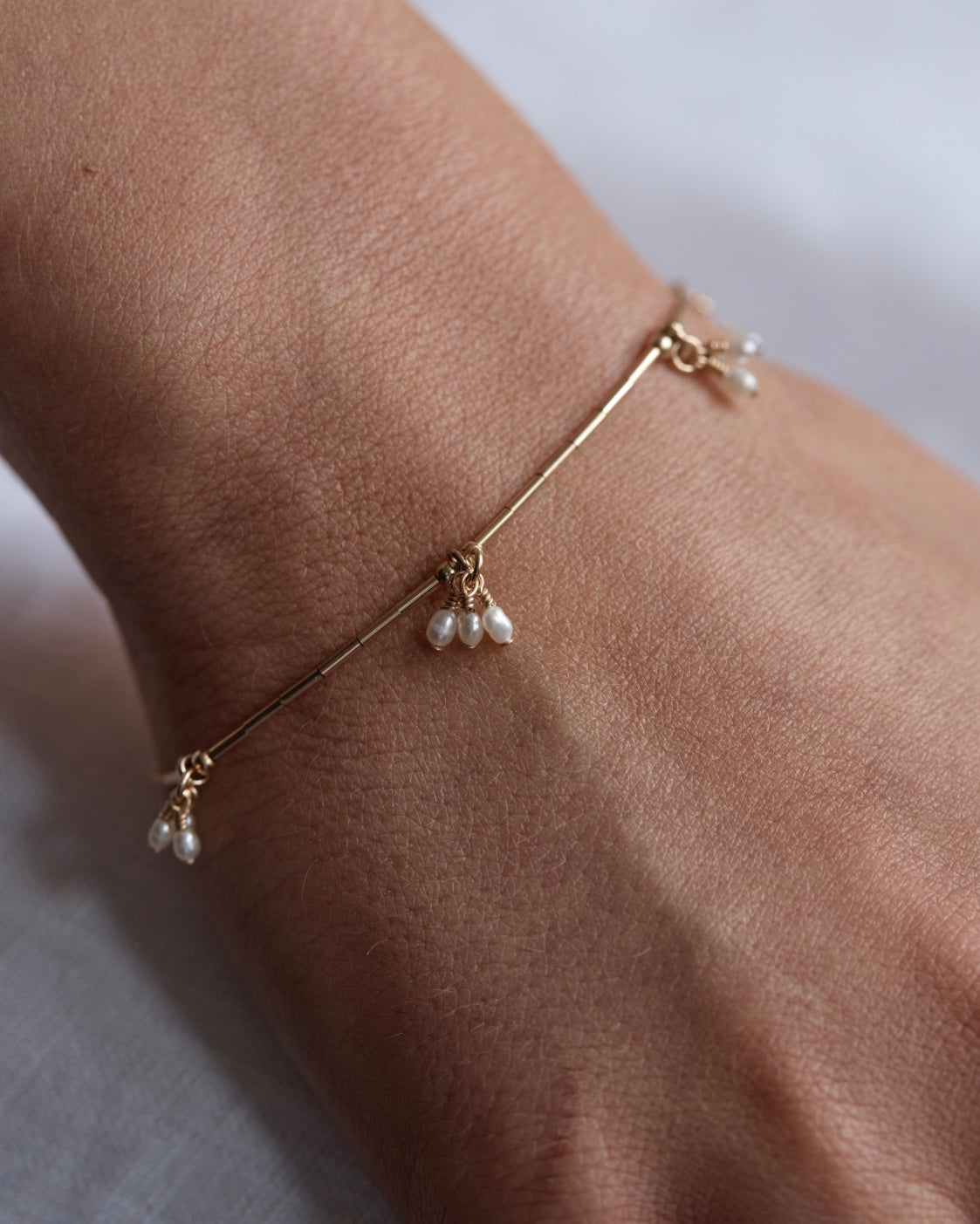 Gold pearl bracelet on a wrist against a neutral background