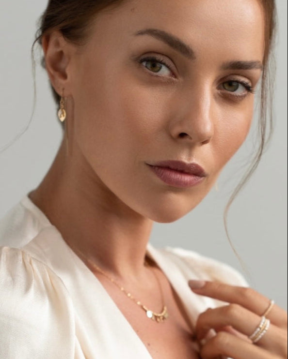 Close-up of a woman wearing gold pearl thread earrings, necklace and rings against a neutral background