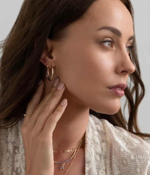 Woman wearing gold hoop earrings and delicate necklaces against a neutral background