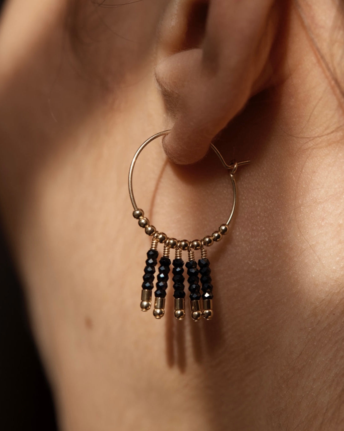 Gold and black spinel hoop earring with gold beads worn on an ear