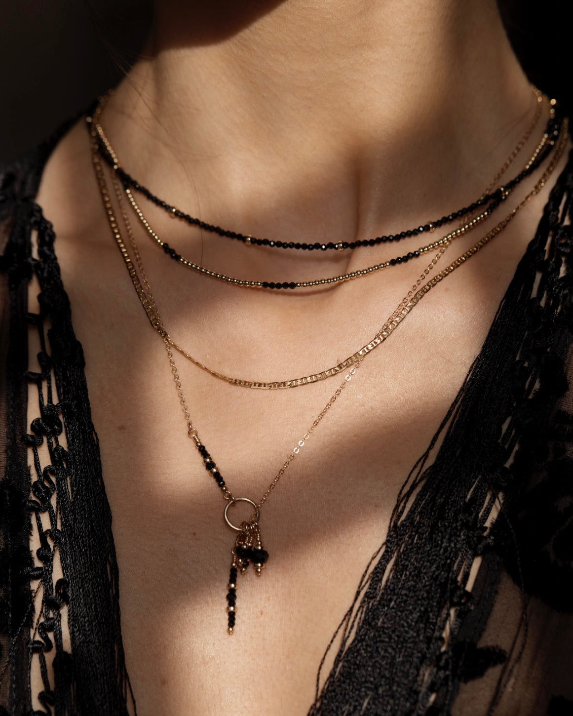 Gold lariat necklace with black onyx and spinel pendant layered with black spinel necklaces worn by a person against a dark background