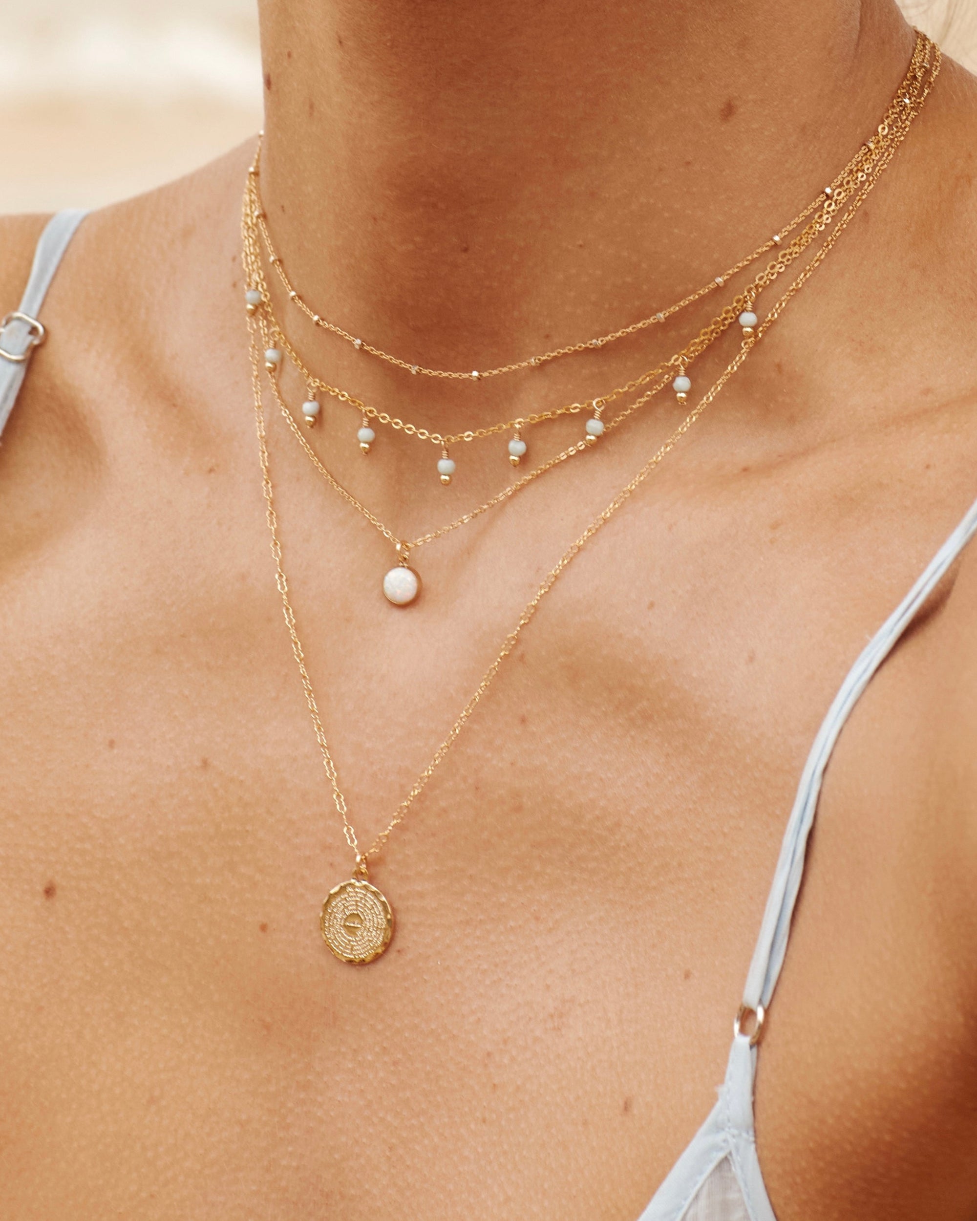 Close-up of a person wearing an opal pendant gold necklace layered with multiple gold necklaces with a blurred background