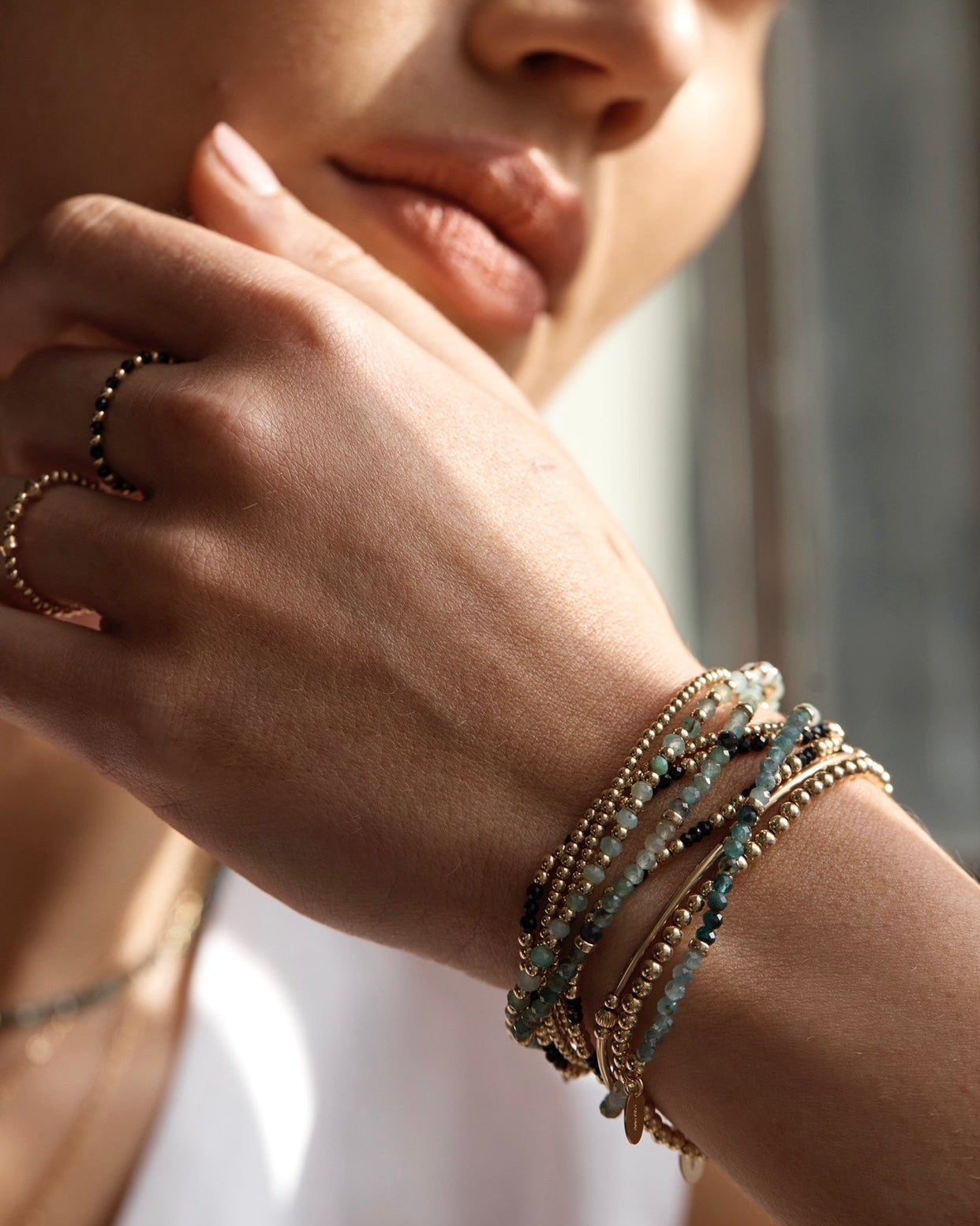 Close-up of a model's wrist with multiple bracelets with grandidierite gemstones  and gold and black spinel gemstone rings.