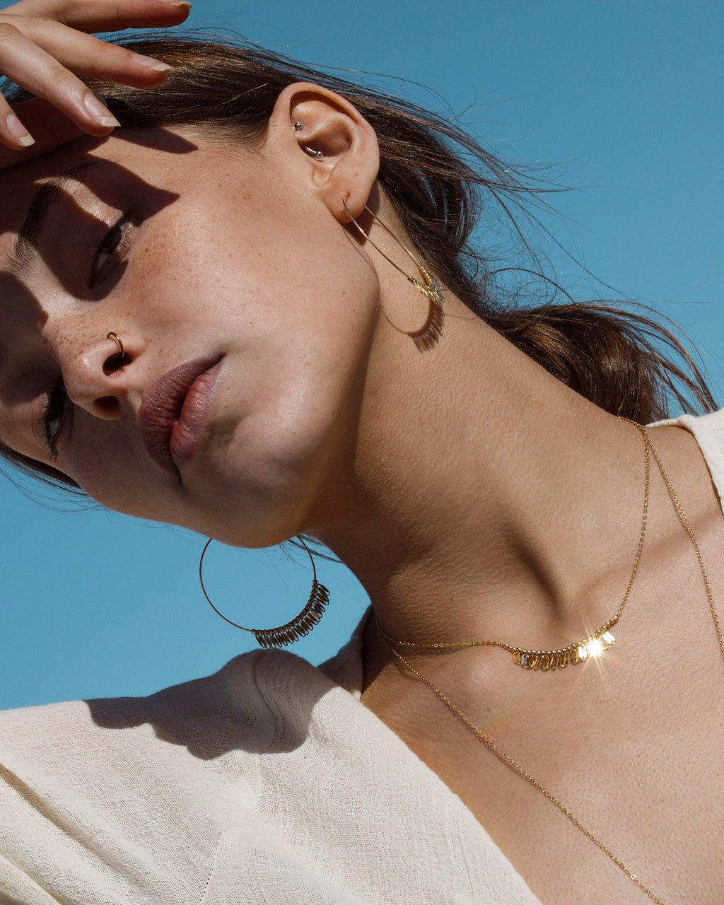 Woman wearing gold necklaces and hoop earrings against a blue sky