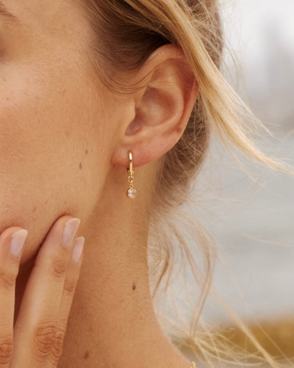 Close-up of a woman wearing a gold cubic zirconia gemstone earring against a blurred background.