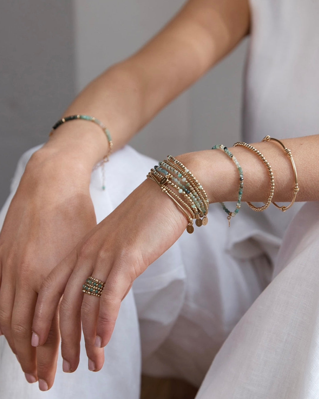 Close-up of a person's wrist with multiple gold emerald gemstone bracelets and rings 