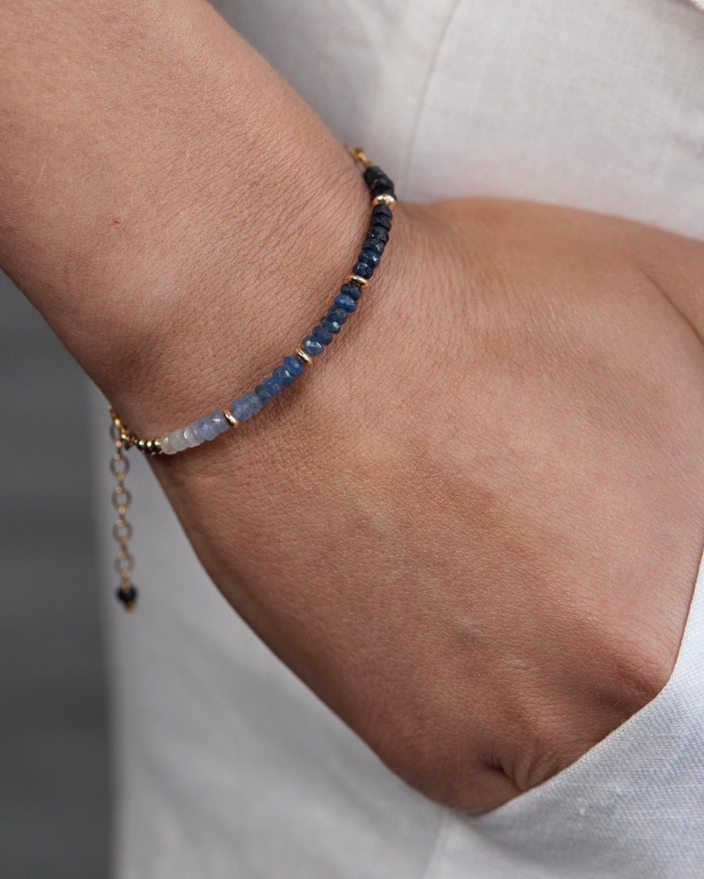Gold bracelet with sapphire gemstones on a wrist against white linen pants.