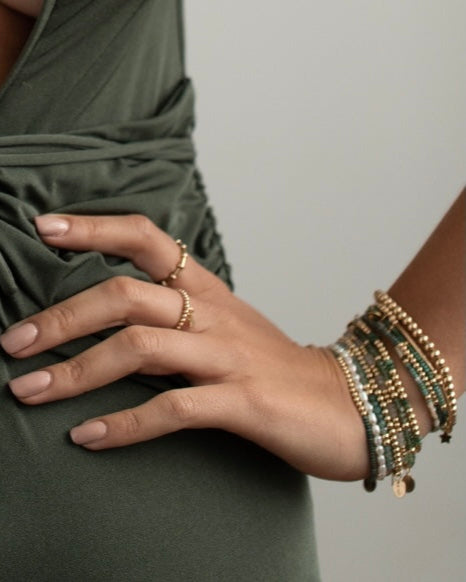 Close-up of a hand and wrist wearing gold rings and bracelets with a plain background