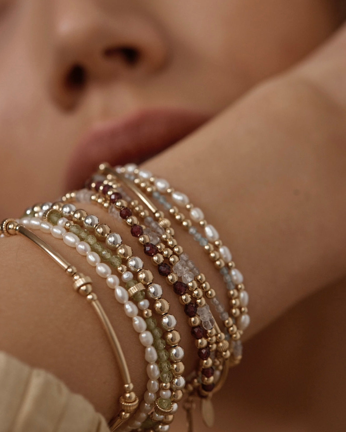 Close-up of a woman's wrist wearing multiple gemstone and pearl beaded bracelets 