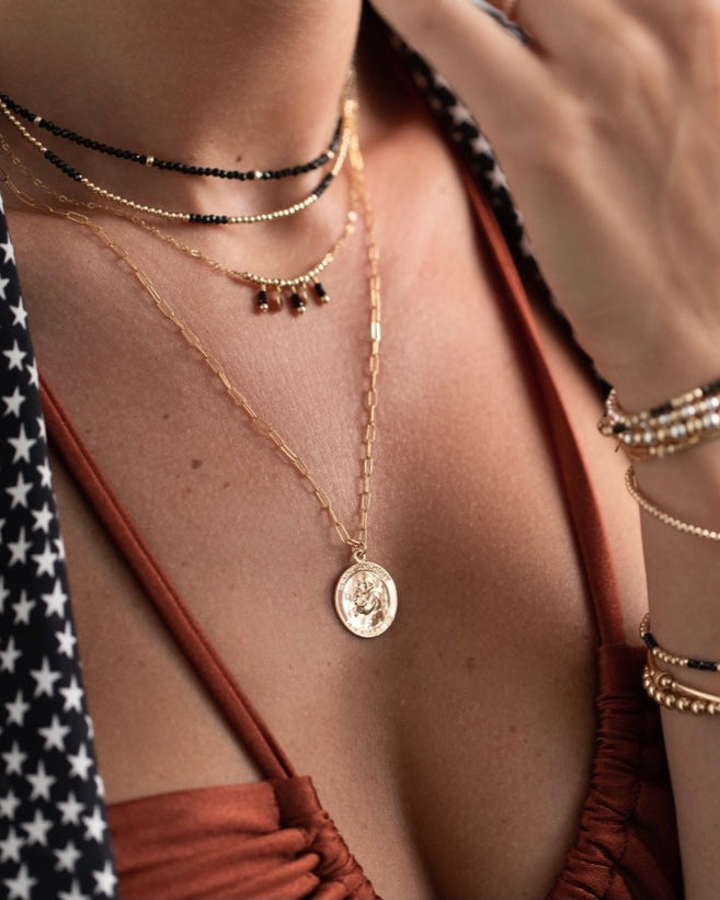 Close-up of a woman wearing multiple 
gold black gemstone necklaces and bracelets 