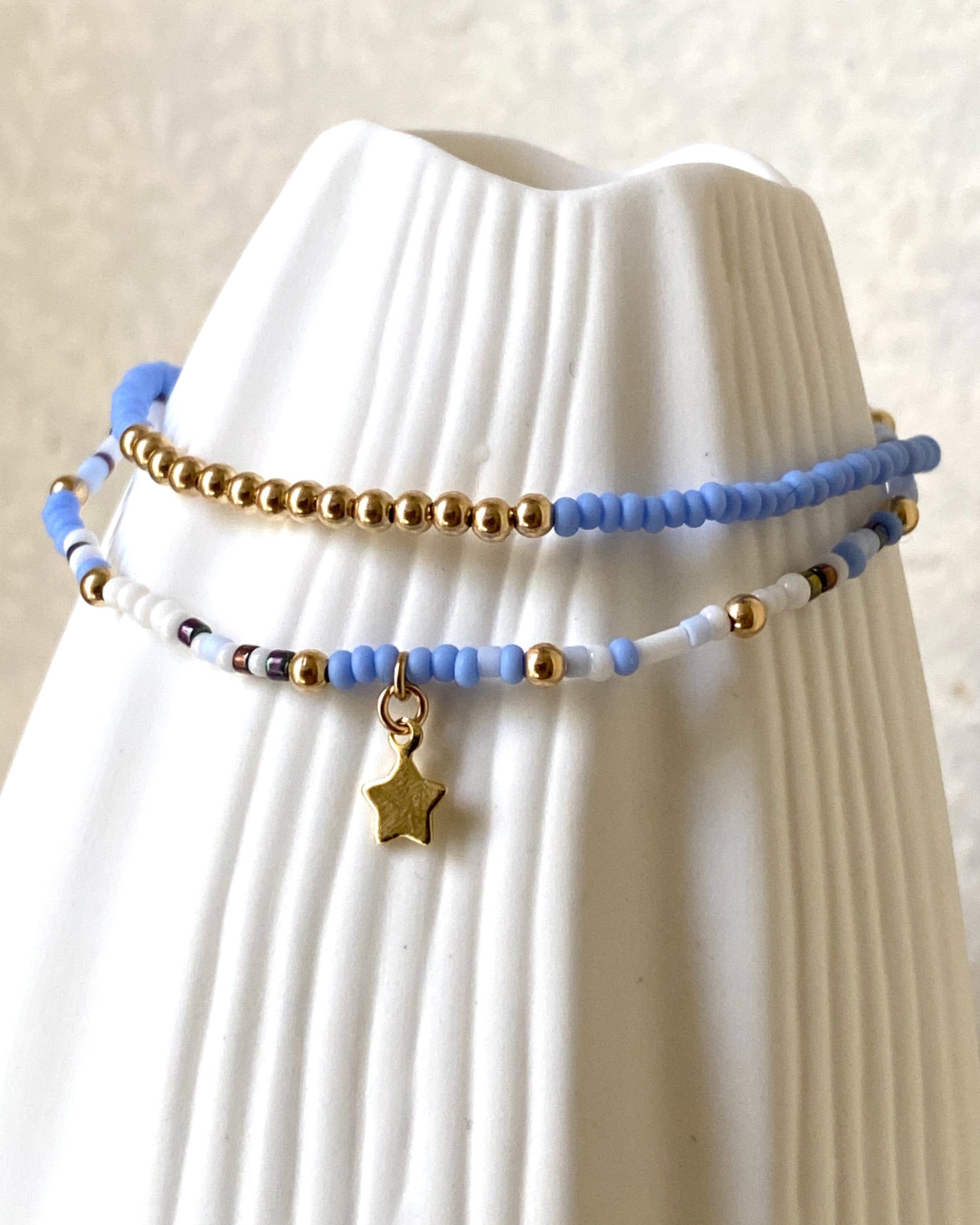 Set of glass and gold beaded bracelets with a star charm on a white prop